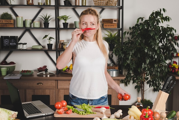 Foto gratuita giovane donna che sta in cucina che odora peperoncino rosso rosso