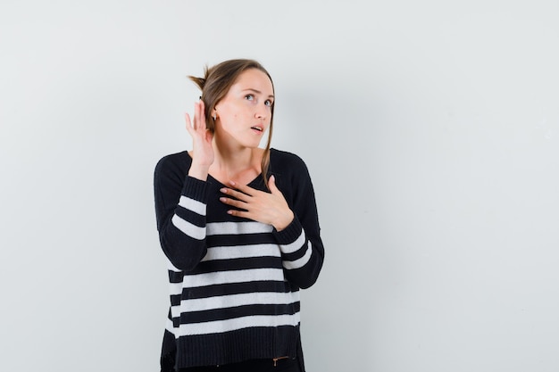 Молодая женщина, стоящая в позе слушателя в полосатом трикотажном белье и черных брюках, выглядит сосредоточенной