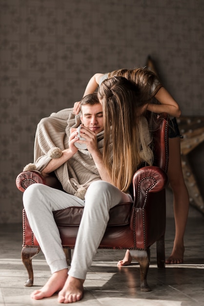 Foto gratuita giovane donna in piedi dietro l'uomo seduto sulla poltrona tenendo la tazza di caffè