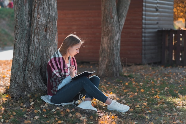 Foto gratuita giovane donna che sta vicino ad un colpo lungo dell'albero