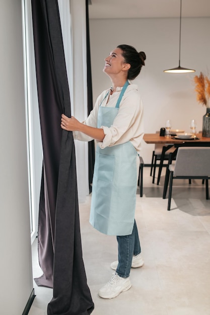 Young woman standing near the widnow and fixing the curtains