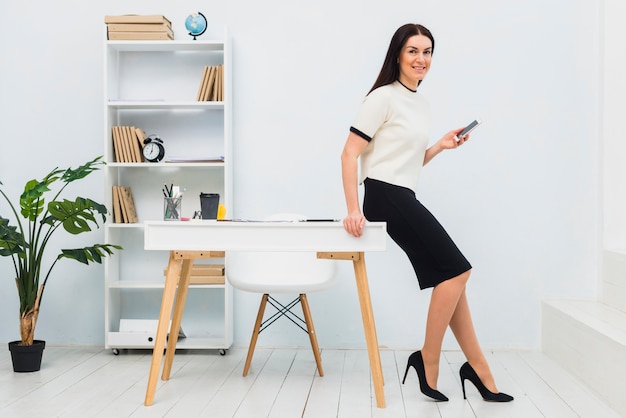 Young woman standing in office with smartphone
