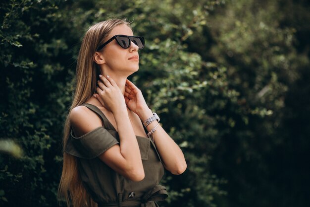 Young woman standing in park on the green bush background