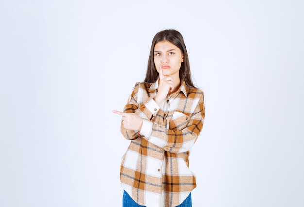 Free photo young woman standing and pointing at her side on white wall.