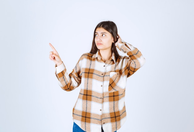 young woman standing and pointing at somewhere on white wall. 