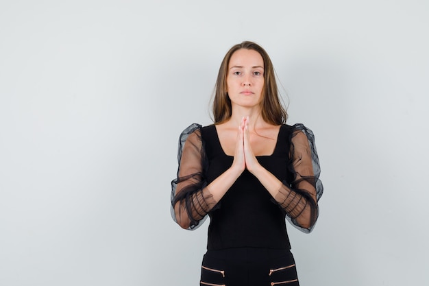 Young woman standing in prayer pose in black blouse and black pants and looking serious. front view.