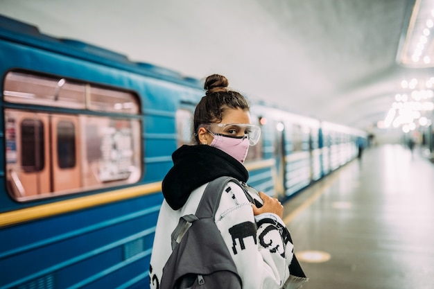 Foto gratuita giovane donna in piedi alla stazione in maschera protettiva medica