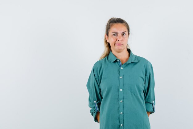 Young woman standing straight, grimacing and posing at front in green blouse and looking pensive