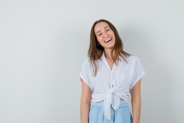 Young woman standing straight and laughing in white blouse and light blue skirt and looking cheerful