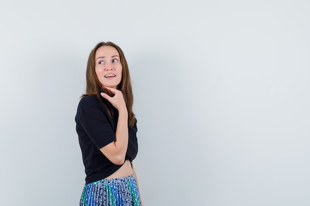 Young woman standing straight and posing at camera while looking away in black t-shirt and blue skirt and looking attractive