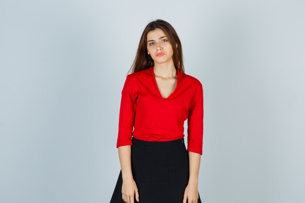 young woman standing straight while posing at camera in red blouse