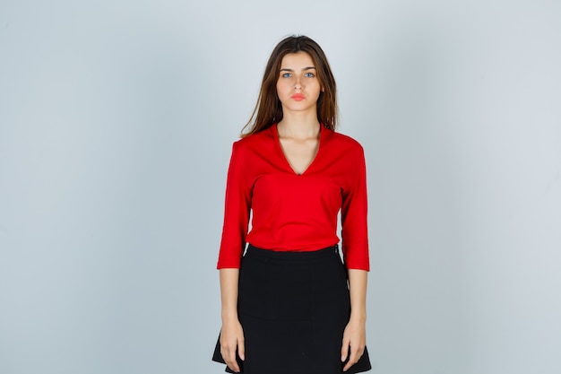 Young woman standing straight while posing at camera in red blouse