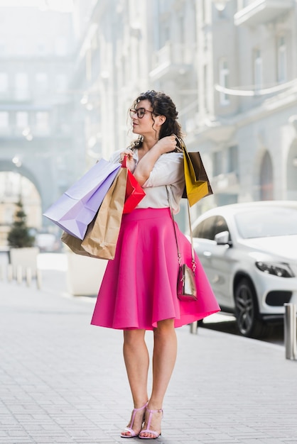 Молодая женщина, стоя на улице с красочными бумажных мешков