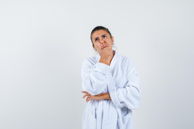 Young woman standing in thinking pose in bathrobe and looking thoughtful