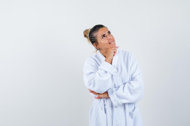 Young woman standing in thinking pose in bathrobe and looking thoughtful