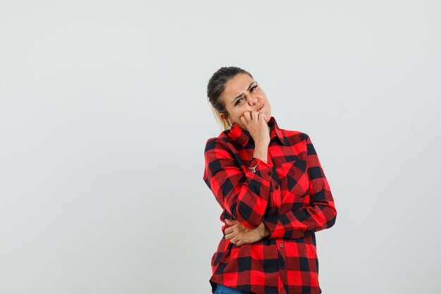 Young woman standing in thinking pose in checked shirt and looking gloomy , front view.