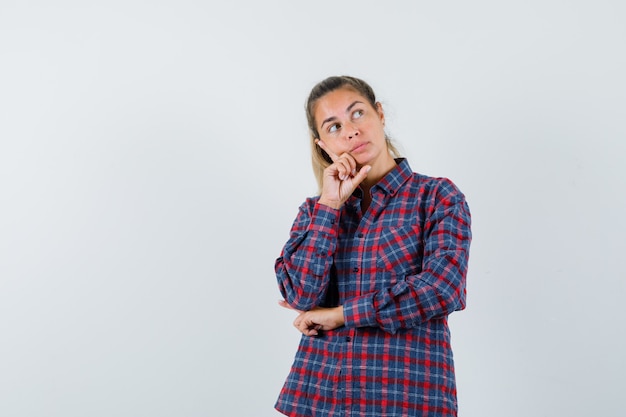 Young woman standing in thinking pose in checked shirt and looking pensive