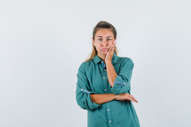 Young woman standing in thinking pose in green blouse and looking pensive