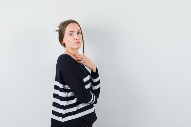 Young woman standing in thinking pose and looking over shoulder in striped knitwear and black pants and looking confident