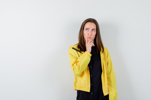 Young woman standing in thinking pose and putting index finger near mouth