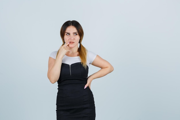 Free photo young woman standing in thinking pose and putting index finger near mouth