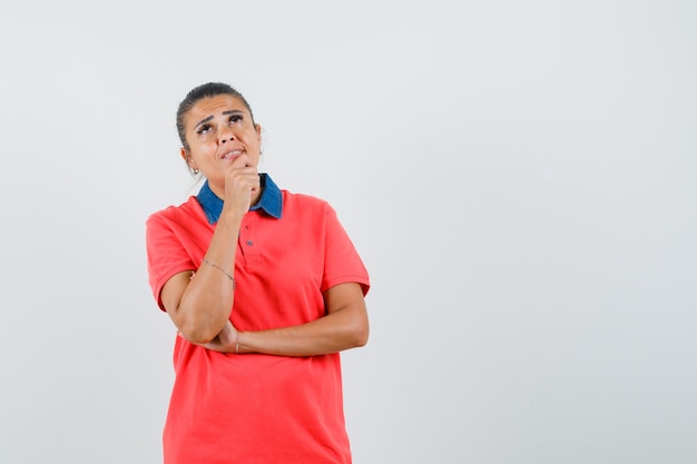 Young woman standing in thinking pose in red t-shirt and looking pensive. front view.