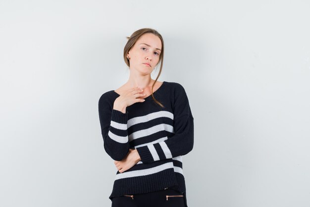 Young woman standing in thinking pose in striped knitwear and black pants and looking pensive