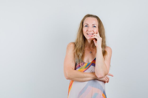 Young woman standing in thinking pose in summer dress and looking cheery. 