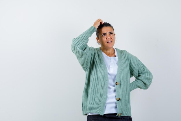 Young woman standing in thinking pose in white shirt and mint green cardigan and looking pensive