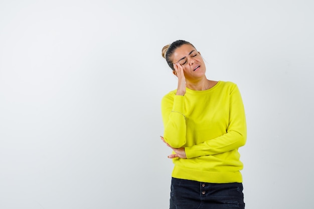 Young woman standing in thinking pose in yellow sweater and black pants and looking pensive