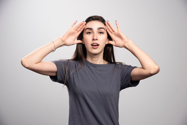 Young woman standing and touching her head over a gray background .