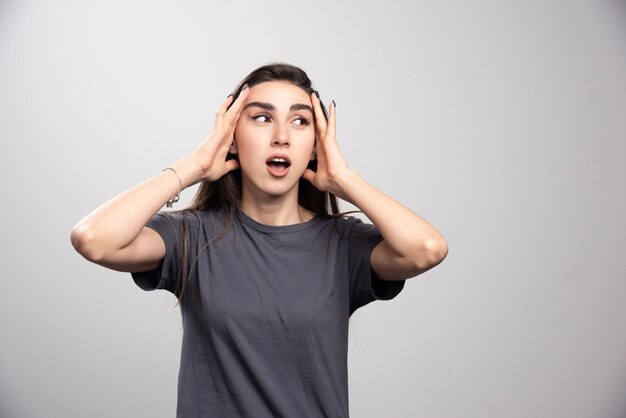 Young woman standing and touching her head over a gray background .