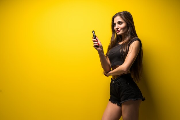 Young woman standing and vaping on yellow wall.