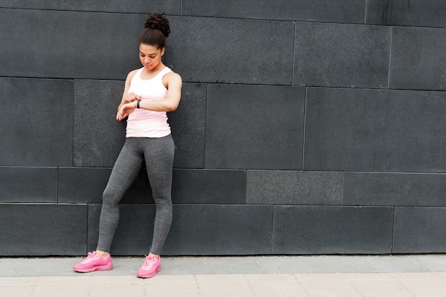 Young woman standing at wall checking activity tracker