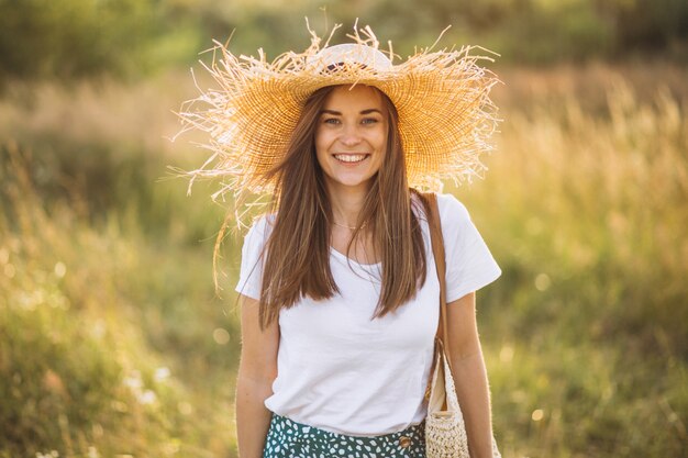 Молодая женщина, стоящая с сумкой в большой шляпе в поле