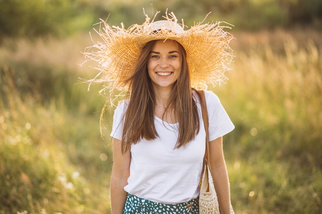 フィールドに大きな帽子のバッグで立っている若い女性