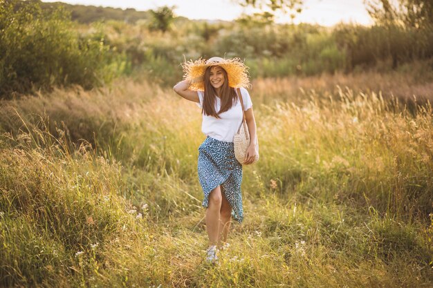 Молодая женщина, стоящая с сумкой в большой шляпе в поле