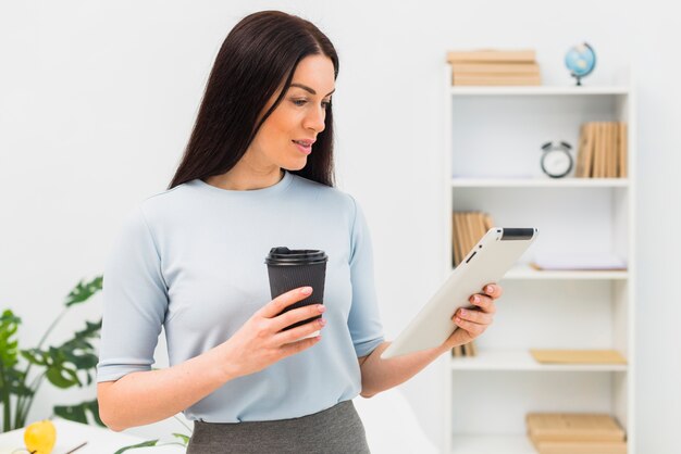 Young woman standing with coffee cup and tablet in office