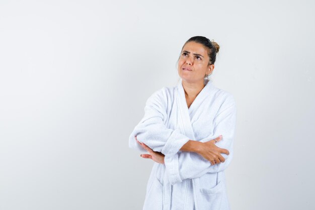 Young woman standing with crossed arms in bathrobe and looking thoughtful