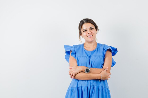 Young woman standing with crossed arms in blue dress and looking cheery