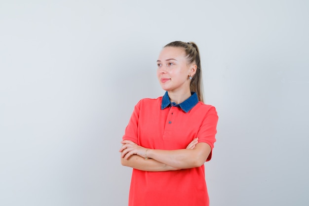 Free photo young woman standing with crossed arms in t-shirt and looking optimistic