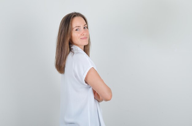 Молодая женщина, стоящая со скрещенными руками в белой футболке и уверенно выглядящая