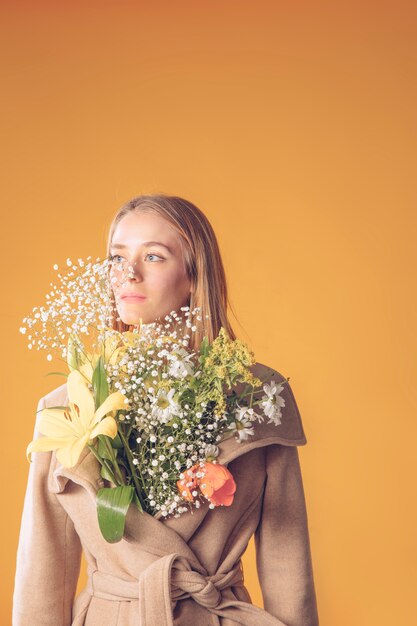 コートの花の花束と立っている若い女性