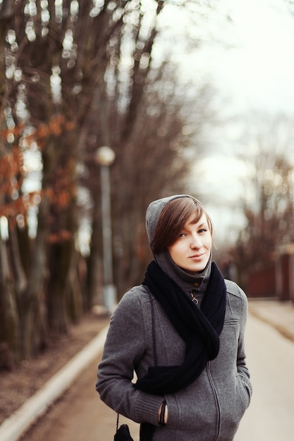 Молодая женщина, стоя с руками в карманах в парке