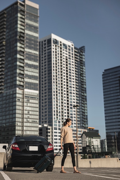 Foto gratuita giovane donna che sta con una valigia nel parcheggio