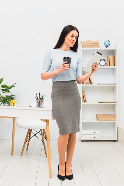 Young woman standing with tablet and coffee cup in office