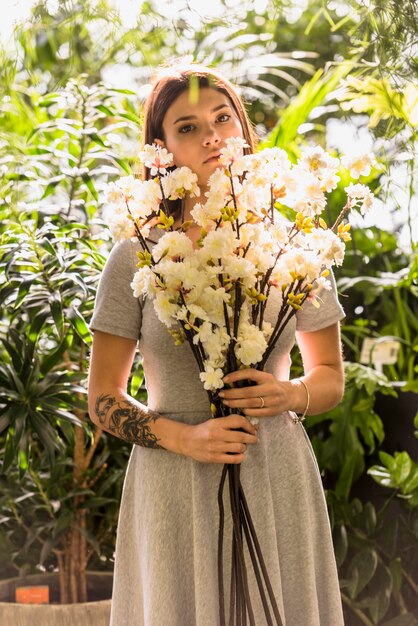 手に白い花で立っている若い女性