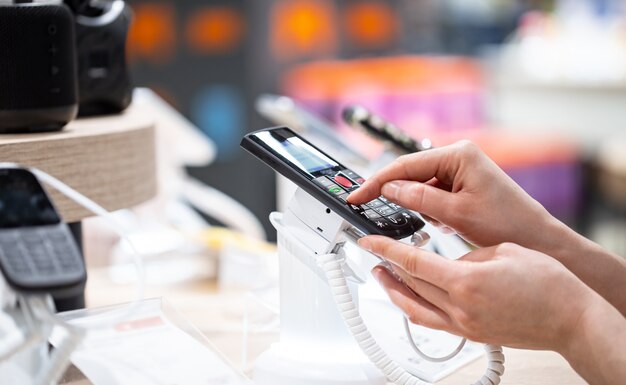 A young woman in the store is standing near the stand and choosing a phone