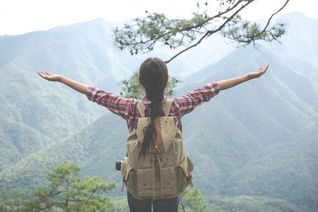 Молодая женщина протянула обе руки к вершине холма в тропическом лесу вместе с рюкзаками в лесу. Приключения, Пеший туризм.