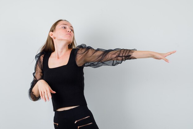 Young woman stretching hand to the right side in black blouse and black pants and looking regretful 